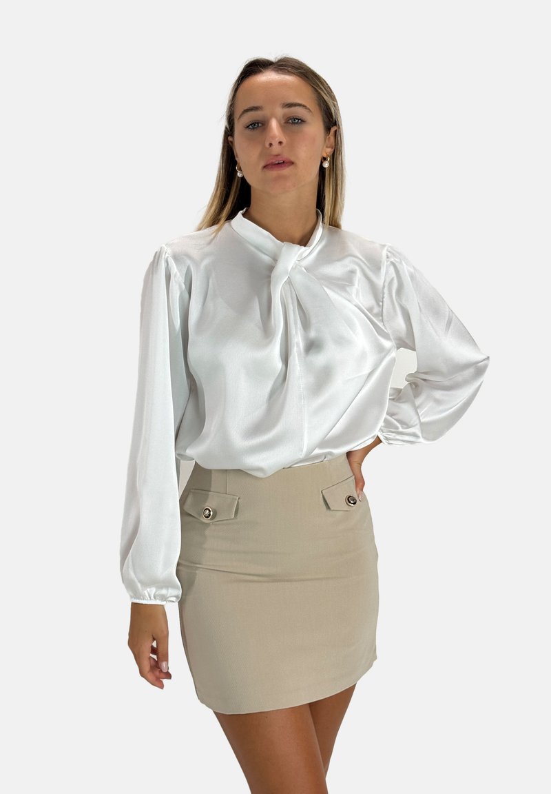 Witte satijnen blouse met een strikdetail bij de hals, ballonmouwen; gecombineerd met een beige minirok met twee voorzakken en knopenaccenten.