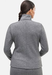 Chaqueta de forro polar gris con un cuello alto, que presenta una textura suave y un diseño ajustado. Detalles de costura que recorren verticalmente la parte posterior.