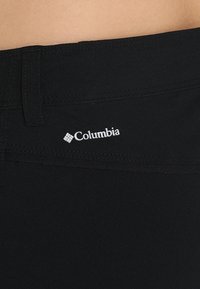 Pantalons noirs avec une texture lisse, présentant un détail de couture à la taille et un logo "Columbia" blanc à l'arrière.