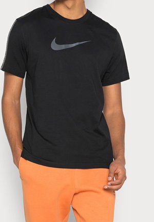 T-shirt en coton noir avec un logo Nike gris sur la poitrine, manches courtes et col rond. Associé à un pantalon de survêtement orange.
