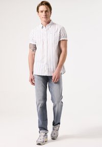 Korte mouw knoopshirt met witte en marineblauwe verticale strepen, gecombineerd met lichtblauwe rechte jeans en lichtgekleurde sneakers.