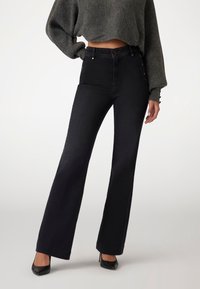 Black, high-waisted jeans with a flared leg, featuring side button accents and a smooth denim texture, paired with a cropped gray sweater.