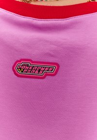 Růžové bavlněné tričko s červeným žebrovaným výstřihem. Obsahuje logo "The Powerpuff Girls" v černé, růžové a žluté barvě.