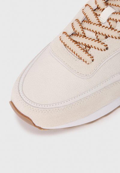 Sneaker bej cu un superior din piele texturată și microsuede, șireturi maro, o talpă intermediară albă și o talpă din cauciuc de tip gumă cu detalii cusute.