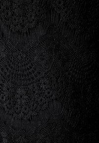 Svart spets tyg med intrikata mönster och texturer. Designen inkluderar öppna vävningar och cirkulära motiv genom hela materialet.