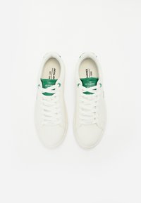 White sneakers with a smooth leather upper, green accents on the tongue and eyelets, and flat white laces. Simple, low-profile design.