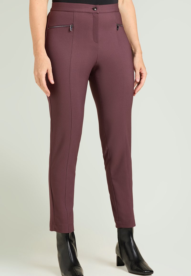 Pantalones ajustados burdeos con textura suave, bolsillos delanteros con cremallera, cintura de tiro medio y diseño de pierna cónica. Combinados con botas negras puntiagudas.