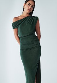 Robe verte à épaules dénudées en tissu doux, avec un design drapé, une fente latérale et des détails froncés pour une silhouette ajustée.