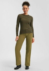 Haut à manches longues en ribbed avec des rayures horizontales vertes et noires, associé à un pantalon taille haute en velours côtelé vert olive et des bottines noires.