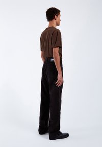 Brown short-sleeve shirt, black corduroy pants, smooth texture, fitted waist, classic design, displayed from the side. Black shoes.