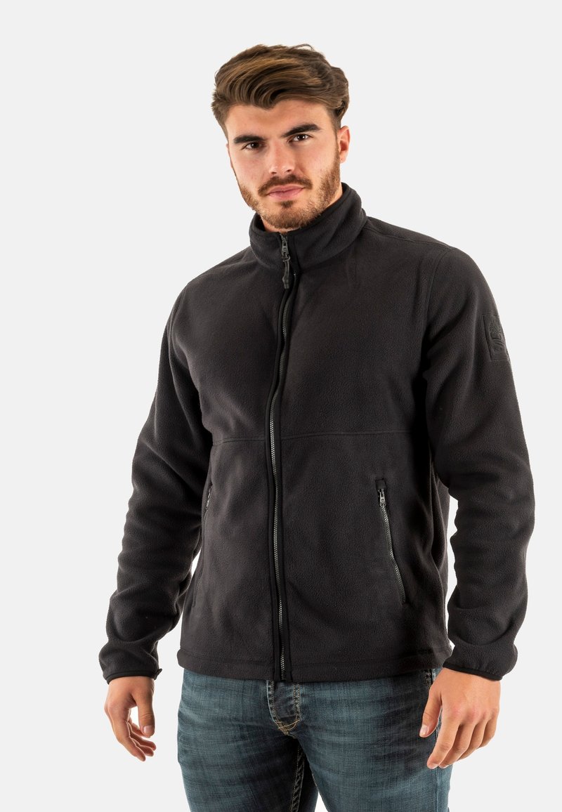 Chaqueta de forro polar negra con un cuello alto, cierre de cremallera frontal y bolsillos laterales. Textura suave, ajuste casual y sin patrones o herrajes visibles.