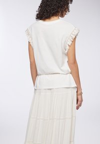 T-shirt bianco in cotone con maniche frangiate e orlo arricciato, abbinato a una gonna fluida color crema con strati sovrapposti e bordo in pizzo.