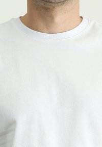 Camiseta de algodón blanca con un diseño clásico de cuello redondo, que presenta una textura suave y una superficie de tela simple y continua.