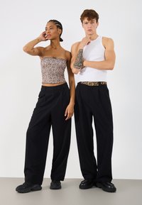 Δύο μοντέλα ποζάρουν φορώντας ρούχα: μια εφαρμοστή τοπ λεοπάρ και μαύρο παντελόνι με φαρδιά πόδια, με μια μαύρη ζώνη που διαθέτει ένα διακριτικό σχέδιο.