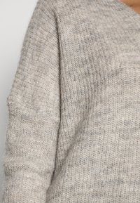 Maglione grigio chiaro a maglia con una texture morbida, caratterizzato da una vestibilità ampia e dettagli a coste lungo i bordi. Il motivo a maglia irregolare aggiunge profondità.