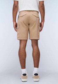 Pantaloni cargo color sabbia con molte tasche laterali, vita aderente e una texture liscia. Abbinati a calze bianche e sneakers beige.
