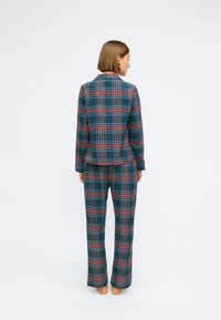 Pyžamový set z bavlneného flanelu s kockovaným vzorom v zelených a námorníckych farbách s červenými a bielymi akcentmi. Voľný strih vršku a široké nohavice.