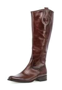 Bottine en cuir marron, montant jusqu'au genou, avec un bout légèrement effilé, une texture lisse et un petit talon empilé. Elle est dotée d'une sangle de traction en haut.