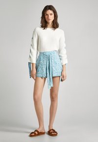 Baltas įrumbuotas megztinis su mėlynais akcentais, derinamas su turkio spalvos raštuotais šortais su kaklaraiščio juosta ir rudiem šlepetėms.