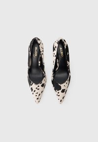 Par de tacones altos ALDO de punta con patrón de estampado de vaca en blanco y negro, vistos desde arriba sobre un fondo liso.