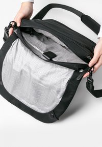 Schwarze Umhängetasche aus glattem Leder, mit einem Reißverschlussverschluss und einem grau gemusterten Innenfutter, das über ein kleines Fach und einen Stoffgurt verfügt.