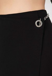 Jupe noire au design épuré, avec un accent circulaire argenté et des détails en chaîne. Fabriquée en tissu lisse et structuré.