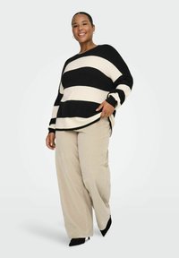 Crna i kremasta prugasta pletena majica opuštenog kroja, s bočnim prorezima i dugim rukavima, uparena s širokim svijetlo bež hlačama i crnim štiklama.