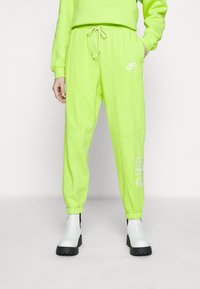 Neongröna sweatpants med elastisk midja och dragsko. Har vita Nike-logotypen och "AIR"-textdetalj på sidan. Avsmalnande ärmslut.