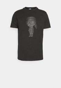 Camiseta negra de manga corta hecha de algodón, con un gráfico metálico de una figura de dibujos animados con gafas de sol y traje en el frente.