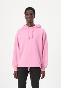 Sweatshirt à capuche rose avec cordon de serrage, manches longues et coupe décontractée. Le tissu semble doux avec une texture lisse ; l'ourlet est légèrement élastiqué.