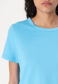T-shirt a maniche corte azzurro chiaro, con scollo rotondo, realizzato in morbido cotone con dettagli di cucitura visibili su maniche e corpo. Texture liscia.