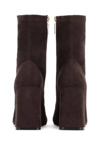 Stivali alla caviglia in suede marrone scuro con tacco a blocco, dotati di zip posteriori, texture liscia e dettagli cuciti sulla parte superiore.