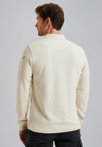 Chemise crème à manches longues avec une finition texturée, dotée d'un col et d'une poche latérale à rabat. Le design est décontracté et ajusté.