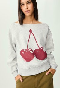 Sweatshirt gris avec un grand motif de cerise bordeaux. Le design a une coupe décontractée avec des poignets et une taille côtelés. Texture douce.