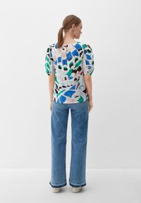 Bunt gefärbte Bluse mit Puffärmeln und abstrakten Mustern in Blau, Grün und Schwarz, kombiniert mit weiten Denim-Jeans und weißen Sneakers.