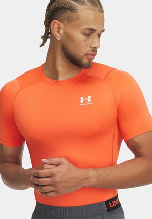 Jasne oranžové športové tričko priliehajúceho strihu s krátkymi rukávmi. Vyrobené z ľahkej, elastickej látky s jemnými detailmi švov a logom Under Armour.