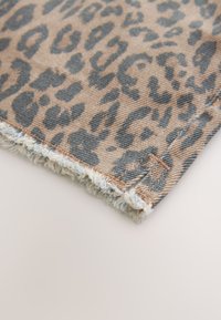 Jeans tkanina z leopardjim vzorcem, s peskovito bež podlago in temnosivimi lisami, s porumenelimi robovi in teksturirano površino.