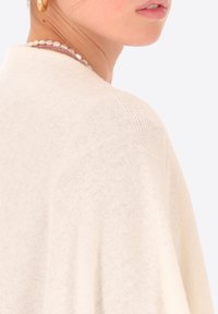 Pullover in maglia beige chiaro con un design morbido e drappeggiato. Presenta un tessuto testurizzato, maniche ampie e un sottile motivo di cucitura.