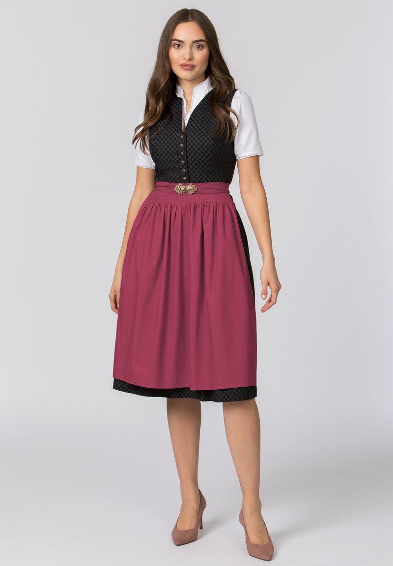 Traditionelles Kleidungsstück mit einer schwarzen gesteppten Weste mit Knöpfen, einer weißen Bluse und einem langen burgunderfarbenen Rock mit gemustertem Saum und dekorativem Gürtel.