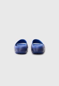Une paire de sandales bleu à enfiler avec des semelles rainurées, montrées de dos sur un fond blanc uni.