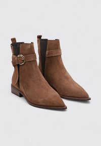 Bottines en suède marron à bout pointu, avec un détail de boucle sur le côté et des panneaux élastiques. Talon plat avec une finition en bois lisse.