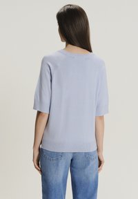 Maglione azzurro chiaro a maglia con maniche corte, orlo a coste e dettagli delle maniche raglan. Indossato con jeans azzurro chiaro a vestibilità ampia.