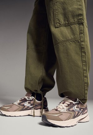 Piedi che indossano sneaker in mesh beige e marrone abbinate a pantaloni cargo verde oliva larghi con coulisse alle caviglie.