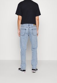 Jeans de mezclilla azul claro con un corte relajado, con bolsillos traseros y una cinturilla de marca, combinados con una camiseta corta negra.