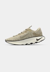 Beige atletiske sko med en tekstureret mesh-overdel, buet hvid mellemsål, sort sål og et subtilt camouflage-mønster. Har snørebånd og øjer.