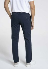 Chinos navy avec une coupe slim, dotés de détails subtils sur les poches arrière et d'une texture lisse, associés à des baskets blanches.