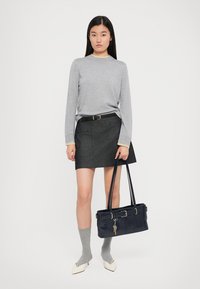 Grauer Langarmpullover, dunkler Rock mit Taschen, graue kniehohe Socken, weiße spitze Schuhe und eine dunkle Handtasche mit einem Schlüsselanhänger.