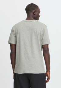 Camiseta gris de manga corta, hecha de una suave mezcla de algodón, con un escote redondeado y un corte relajado, vista desde atrás.