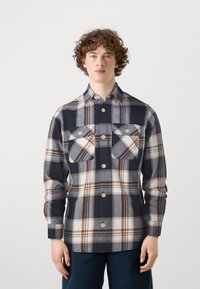 Camisa de cuadro en azul marino y gris, hecha de una tela de textura suave, que cuenta con cierres de botones y dos bolsillos en el pecho con solapas.