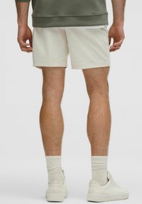 Witte shorts voor mannen van een gladde, lichte stof, gecombineerd met lichtgekleurde sneakers en geribbelde sokken, gezien vanuit de achterkant.